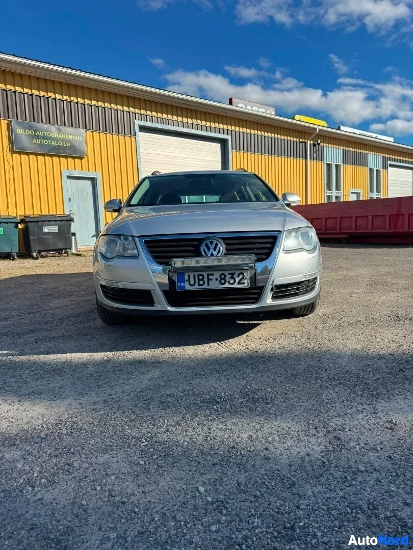 Edestä: Hopeanvärinen farmariauto kuvattuna edestäpäin sorapihalla rakennuksen edessä. Auton etupuskurissa on lisävalo.
