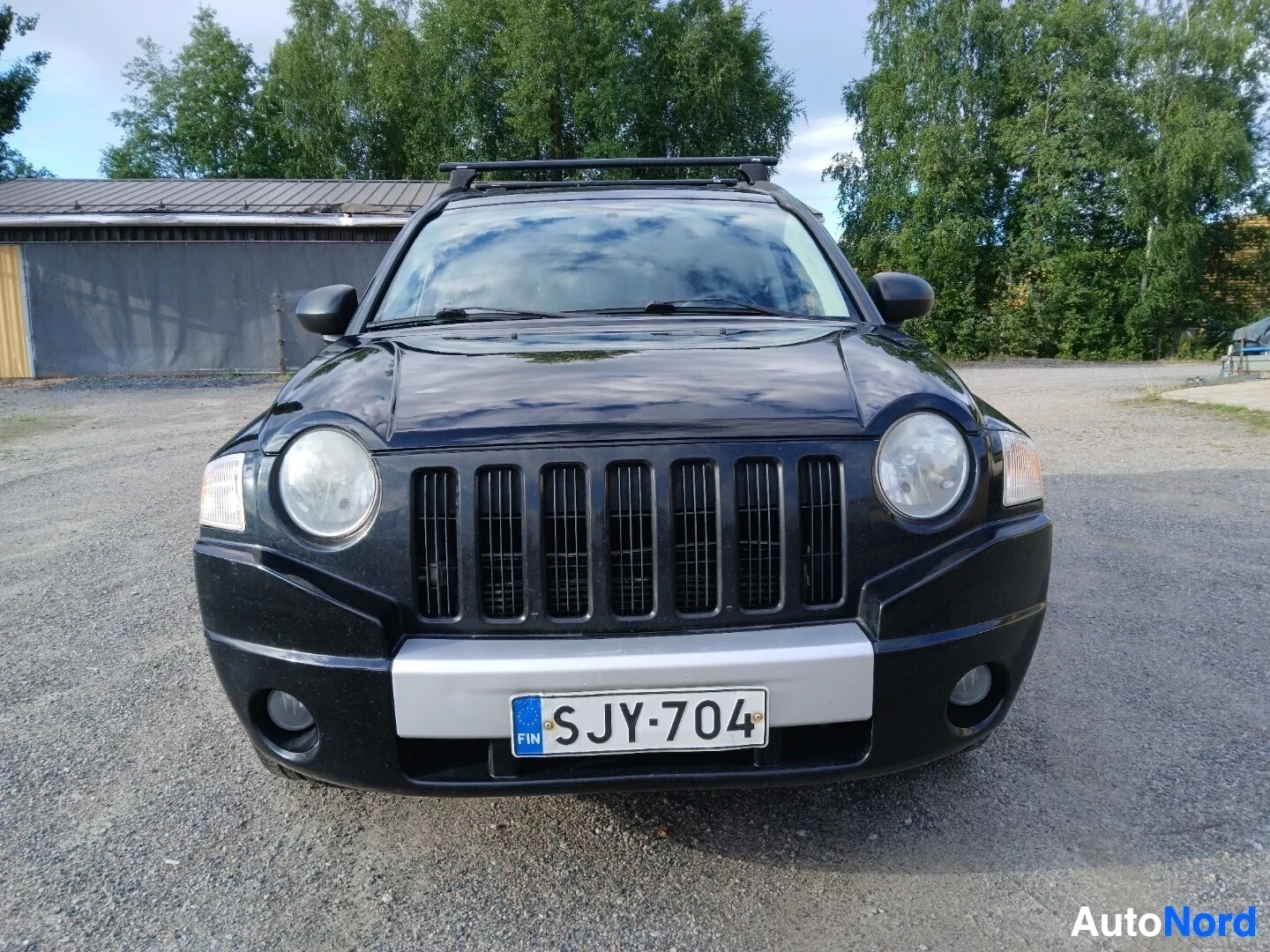 Edestä: Musta Jeep Compass edestäpäin kuvattuna. Autossa on kattotelineet ja suomalainen rekisterikilpi