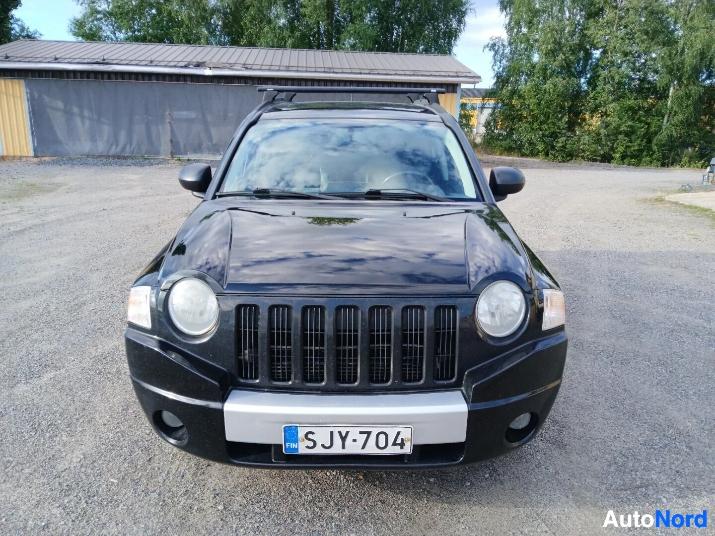 Edestä: Musta Jeep Compass edestäpäin kuvattuna. Autossa on kattotelineet ja suomalainen rekisterikilpi