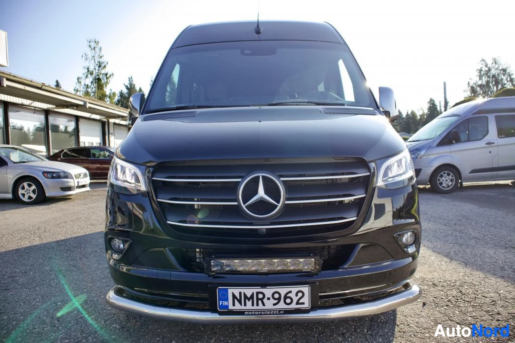 Edestä: Musta pakettiauto edestäpäin kuvattuna. Keulassa on kromatut yksityiskohdat ja etupuskurissa lisävalopalkki. Ajoneuvon rekisterikilpi on "".