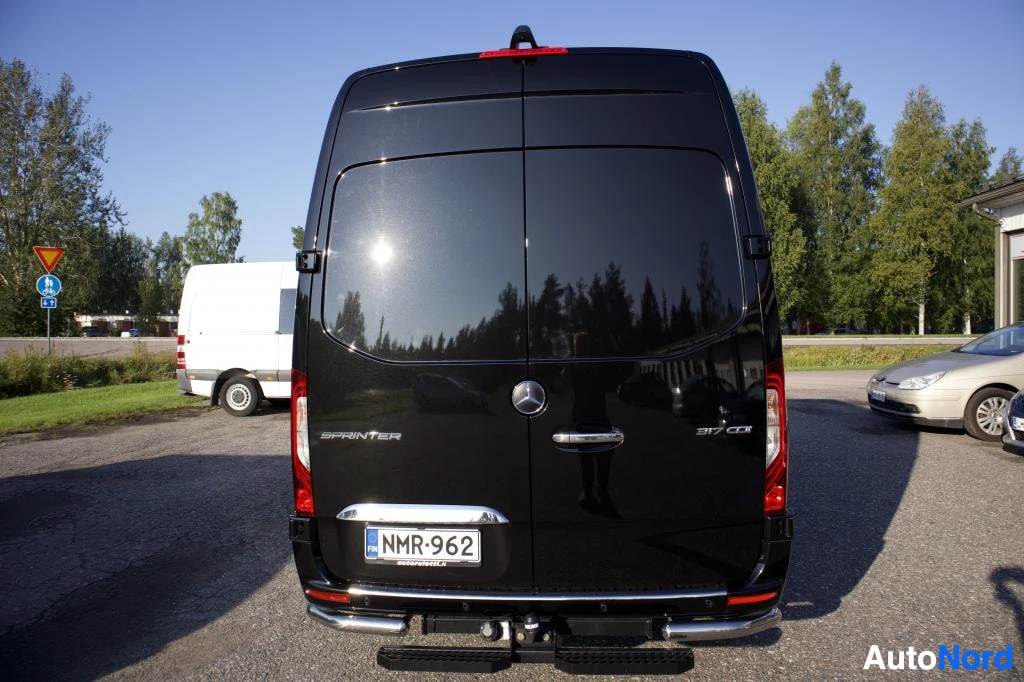 Takaa: Musta pakettiauto, jossa on takaluukku ja tummennetut takaikkunat, on pysäköity ulos. Ajoneuvon perä on näkyvissä.