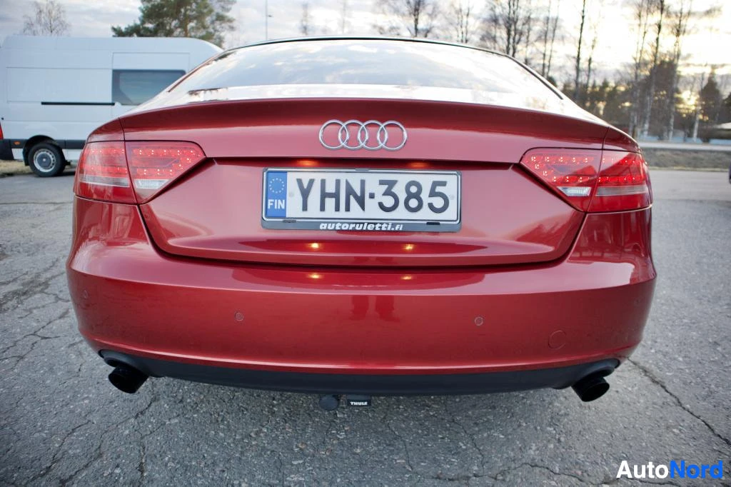 Takaa: Punaisen Audi A5 Sportbackin takaosa on kuvattu suoraan takaa. Rekisterikilpi on näkyvissä. Puskurissa on kaksi tutka-anturia ja puskurin alla on Thule-merkkine