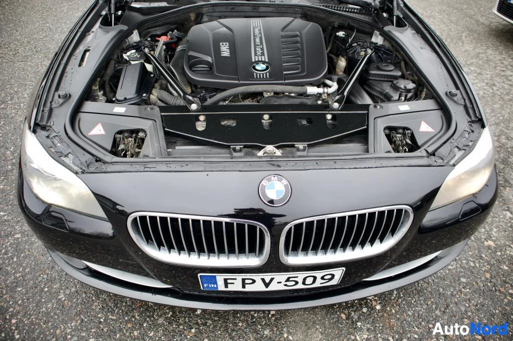 Moottoritila: Lähikuva avatusta moottoritilasta, jossa BMW-moottori on näkyvissä. Edessä on auton keula ja rekisterikilpi.
