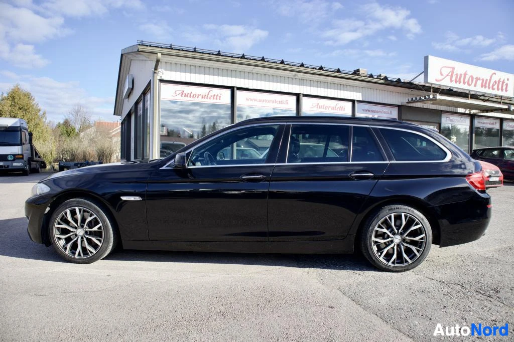 Sivulta: Musta BMW 5-sarjan farmari kuvattuna oikealta sivulta. Katto, kattokaiteet ja molemmat sivupeilit ovat näkyvissä. Autossa on monipuolaiset kevytmetallivanteet e