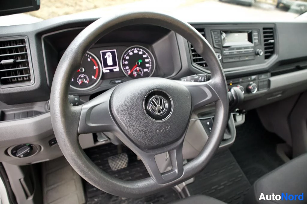 Ohjaamo: Lähikuva kuljettajan paikalta, jossa näkyy auton ohjauspyörä Volkswagen-logolla, mittaristo ja radio/soitin.