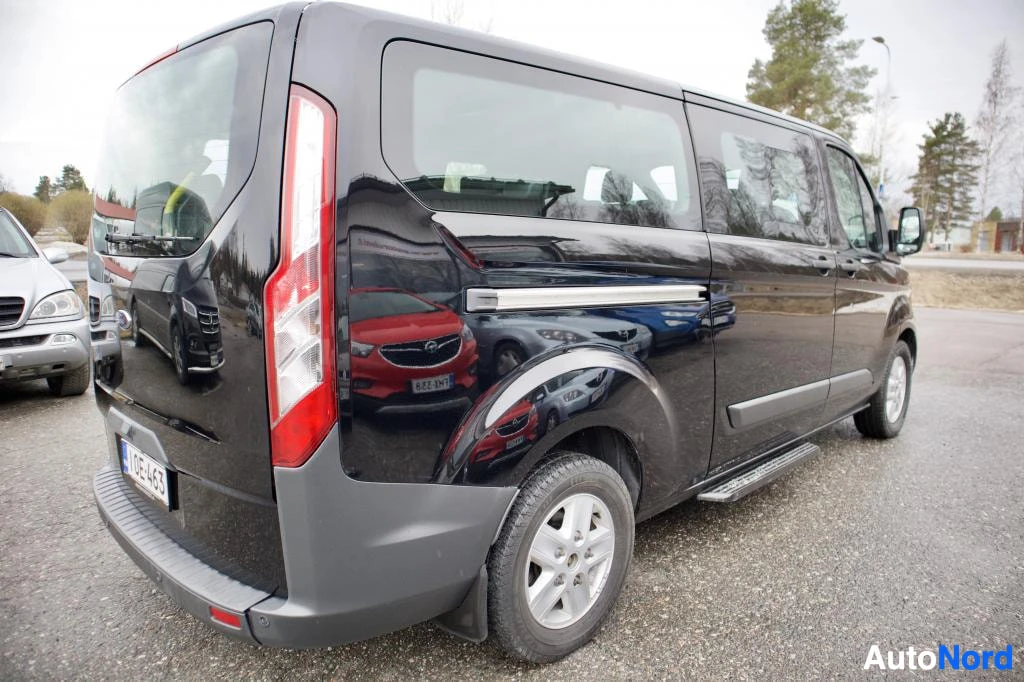 Takaviisto: Musta pakettiauto, jossa on alumiinivanteet ja astinlaudat, pysäköitynä takaviistosta kuvattuna. Rekisterikilpi "" on osittain näkyvissä