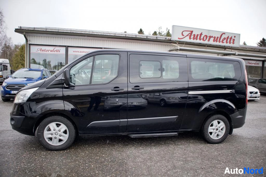 Sivulta: Musta pakettiauto, jossa on harmaat peltivanteet, seisoo ulkona sivuprofiilissa. Kyljen ja ikkunoiden heijastukset vääristävät kuvaa. Auton sivuovi ja takaovi o