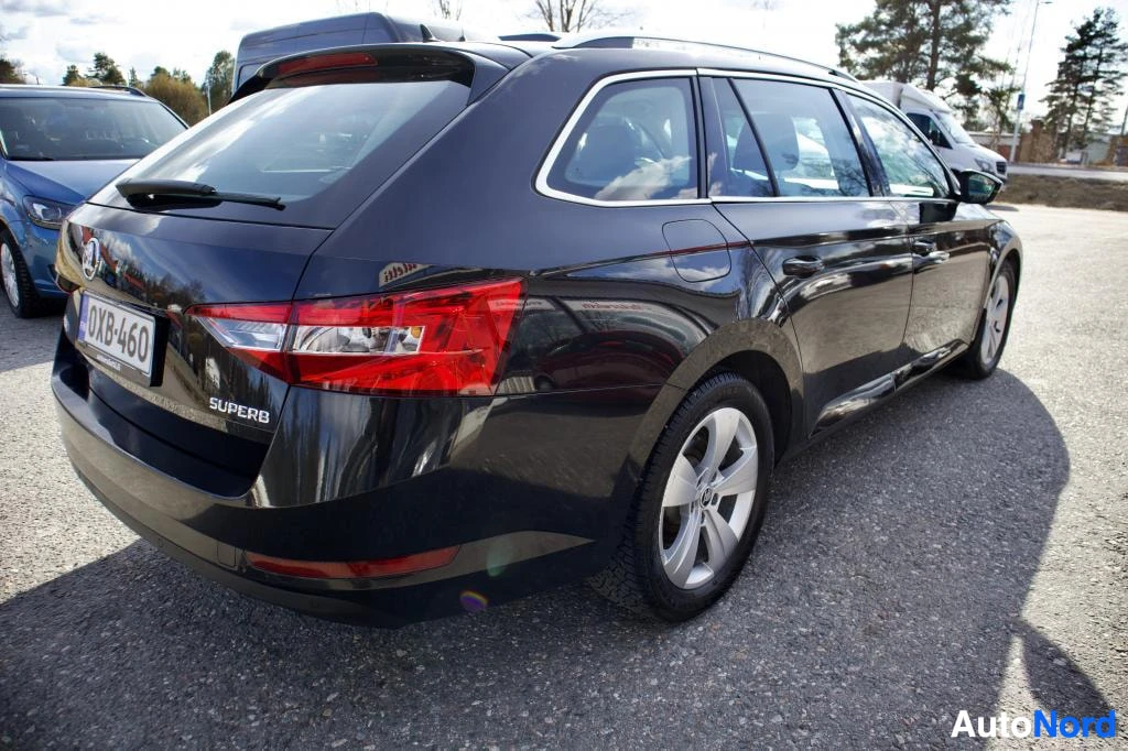 Takaviisto: Musta Skoda Superb -farmariauton takaosa, jossa näkyvät takavalot, takaluukku ja "SUPERB"-merkki. Rekisterikilpi "" on takaluukussa
