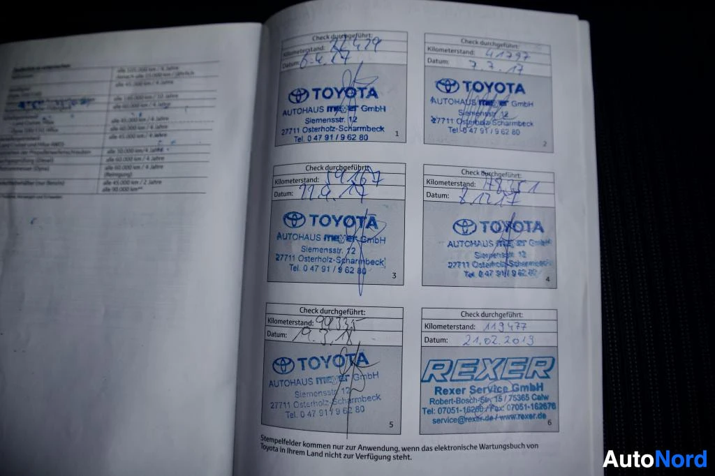 Yksityiskohta: Avatun huoltokirjan sivuja, joilla useita leimoja ja käsinkirjoitettuja merkintöjä. Näkyvissä kilometrilukemat, päivämäärät ja TOYOTA Autohaus Meyer GmbH -leimo