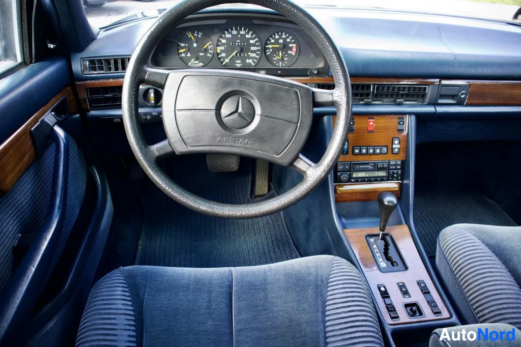 Ohjaamo: Kuvakulma kuljettajan istuimelta auton kojelautaan. Kojelautaa hallitsevat mittaristo, ohjauspyörä, jossa lukee "AIRBAG", ja keskikonsoli, jossa on puujäljitelm