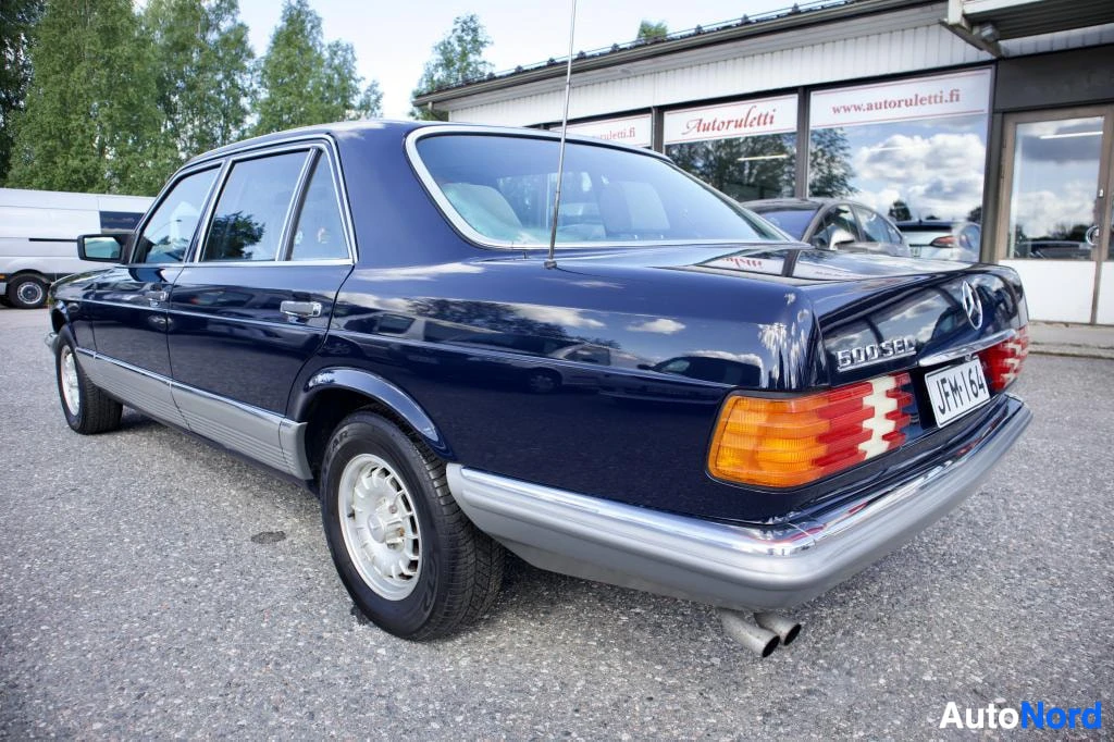 Takaviisto: Tummanpunainen Mercedes-Benz, oikea takakulma kuvattu. Rekisterikilpi "" näkyy. Kyljessä on merkintä "500 SEL"