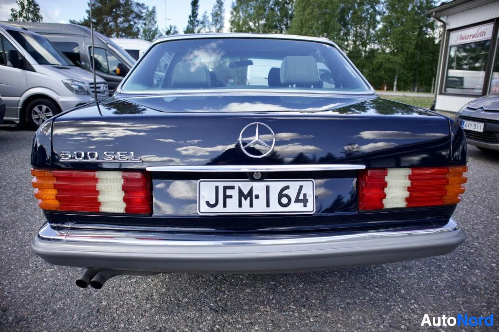 Takaa: Tummanpunaisen Mercedes-Benzin takaosa, rekisterikilvessä teksti "". Takaluukussa on logo ja merkintä "500 SEL"