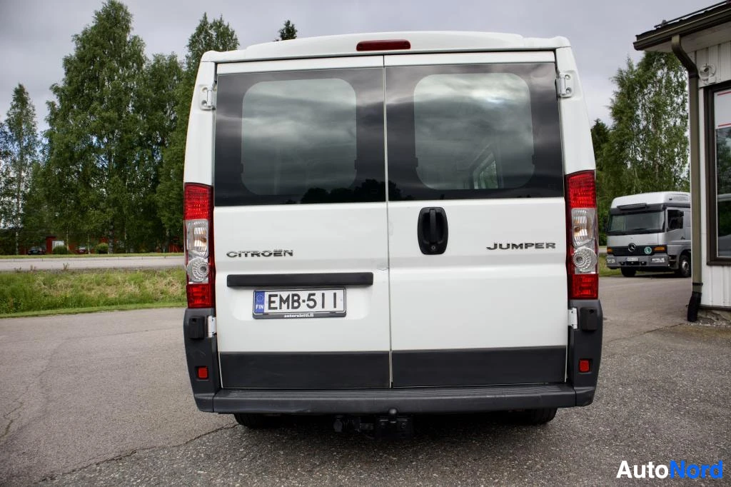Takaa: Valkoisen pakettiauton takaosa, jossa on rekisterikilpi "" ja perävaunun vetokoukku. Takaluukussa on kaksi ikkunaa ja 'CITROEN' sekä 'JUMPER' -merkit. Kuvassa n