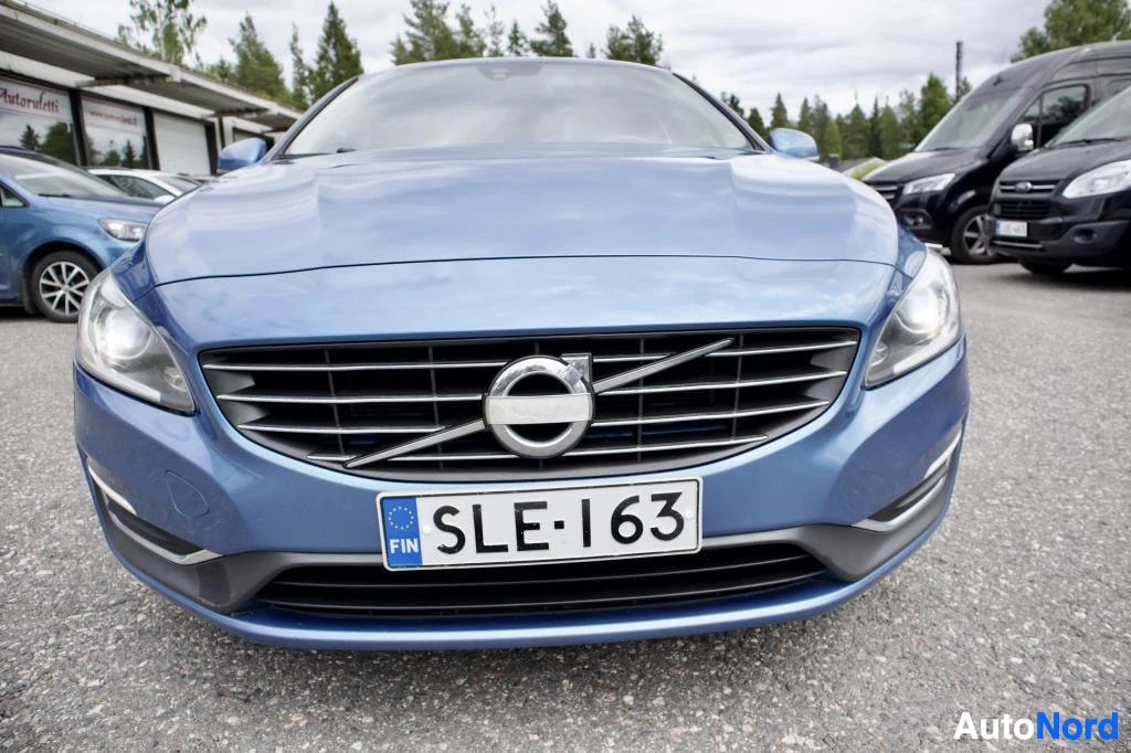 Edestä: Sininen Volvo S60 kuvattuna suoraan edestä. Auton rekisterikilvessä on teksti