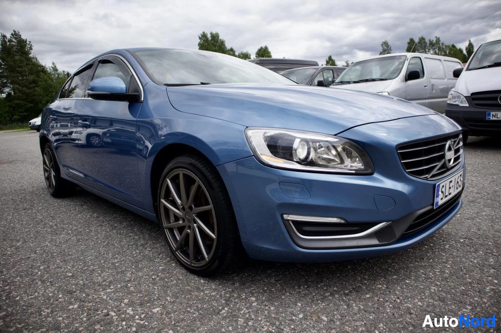 Etuviisto, nokka oikealle: Sininen Volvo S60 etuviistosta vasemmalta edestäpäin kuvattuna parkkipaikalla.