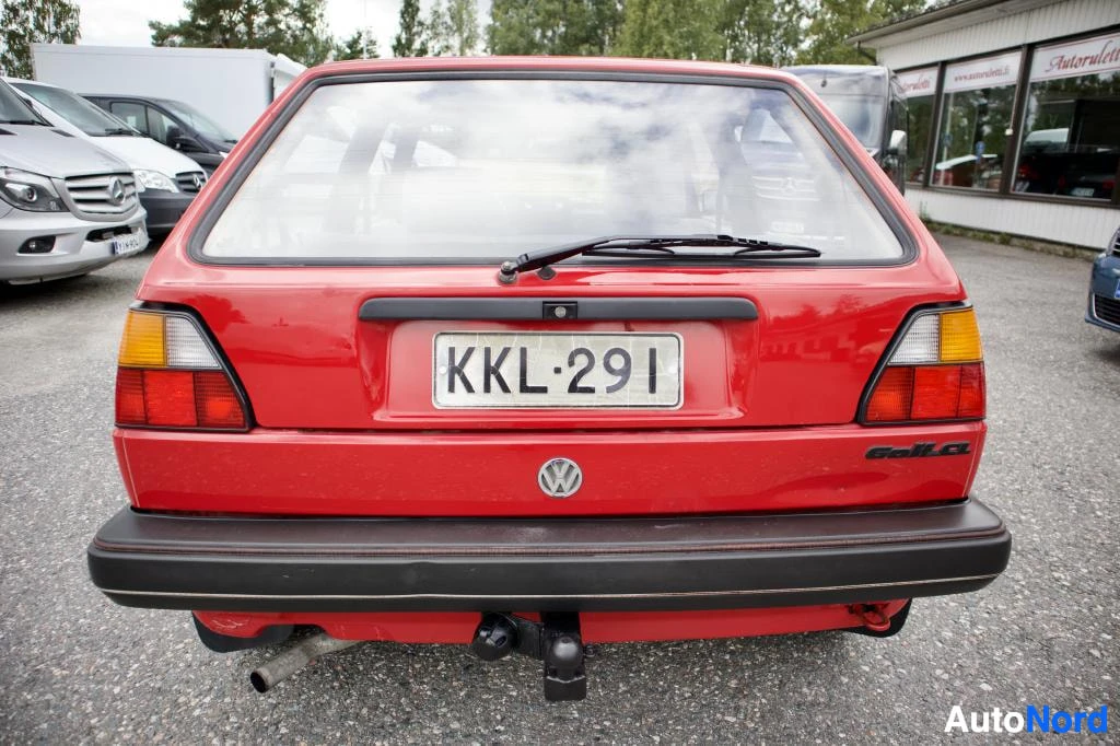 Takaa: Punaisen kaksiovisen Volkswagen Golfin takaosa kuvattuna ulkona parkkipaikalla. Autossa on takalasinpyyhin, vetokoukku ja rekisterikilpi