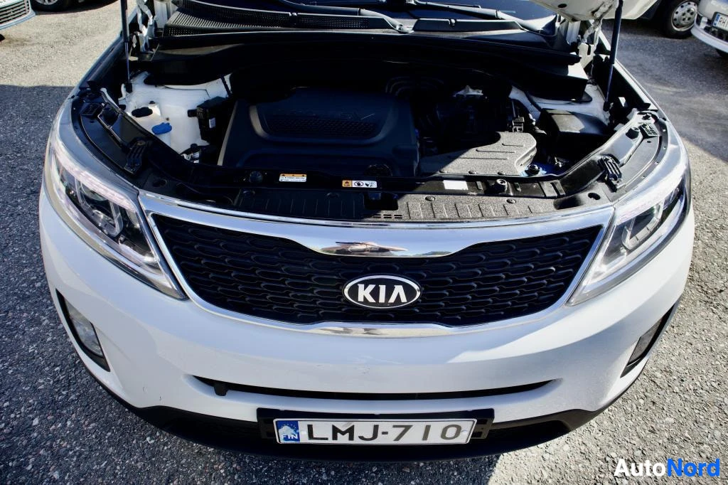 Edestä: Auton konepelti on auki ja moottori on näkyvissä. Edestä kuvatun auton etusäleikkö, jossa on KIA-logo, ja eturekisterikilpi "" ovat myös näkyvissä