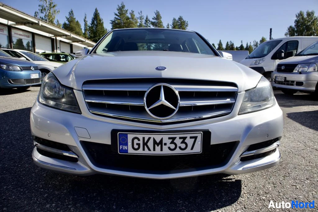 Edestä: Hopeanvärisen Mercedes-Benz C-sarjan sedanin keula edestä päin kuvattuna. Rekisterikilpi on näkyvissä