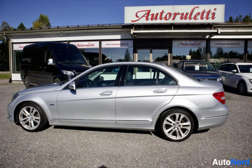 Sivulta: Hopeanvärinen Mercedes-Benz C-sarjan sedan sivusta kuvattuna pysäköintialueella. Auton vieressä on rakennus, jonka katolla on "Autoruletti"-kyltti.