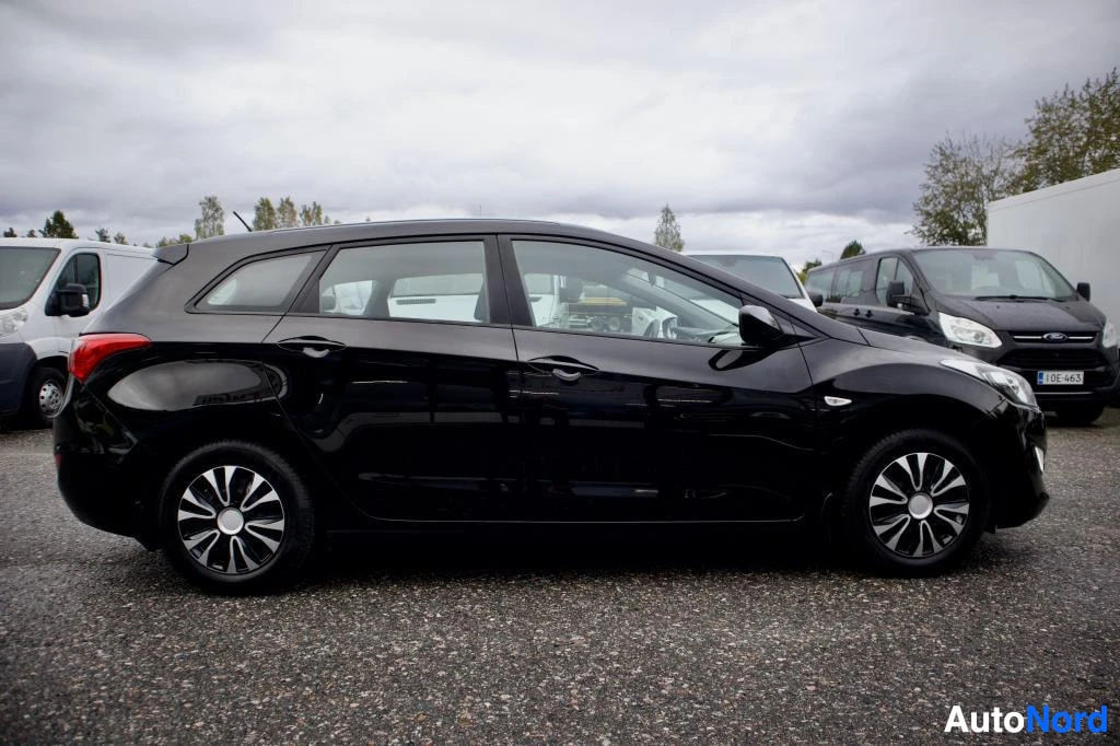 Sivulta: Musta auto kuvattuna oikealta sivulta. Auto on pysäköity asfalttipihalle. Kevytmetallivanteet näkyvät molemmissa renkaissa.
