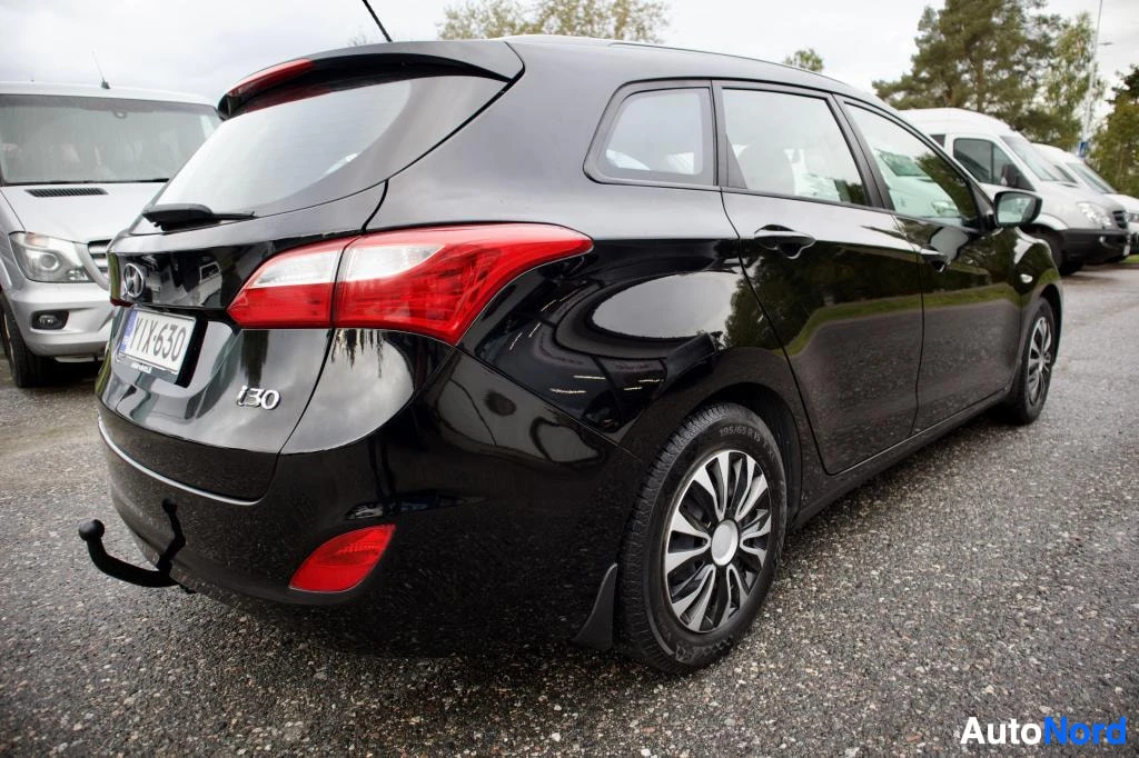 Takaviisto: Musta Hyundai i30 -farmariauto kuvattuna takavasemmalta viistosta ulkona pysäköintialueella. Autossa on vetokoukku.