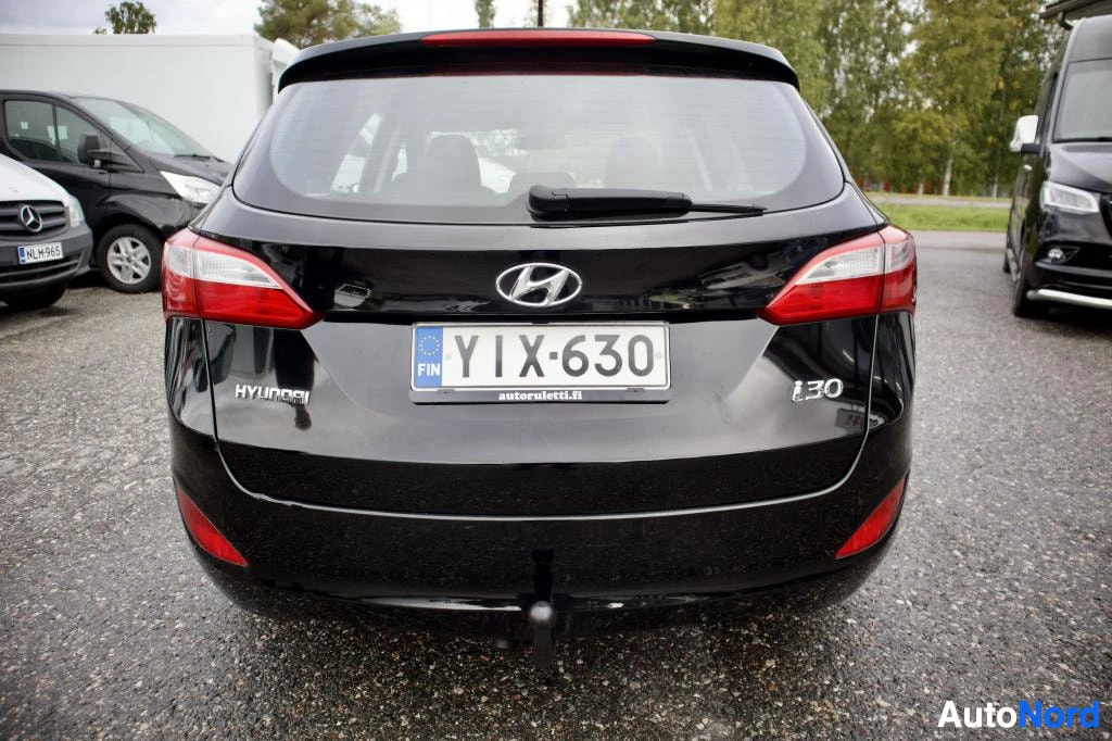 Takaa: Musta Hyundai i30 -farmariauto kuvattuna suoraan takaa ulkona pysäköintialueella. Autossa on vetokoukku ja rekisterinumero