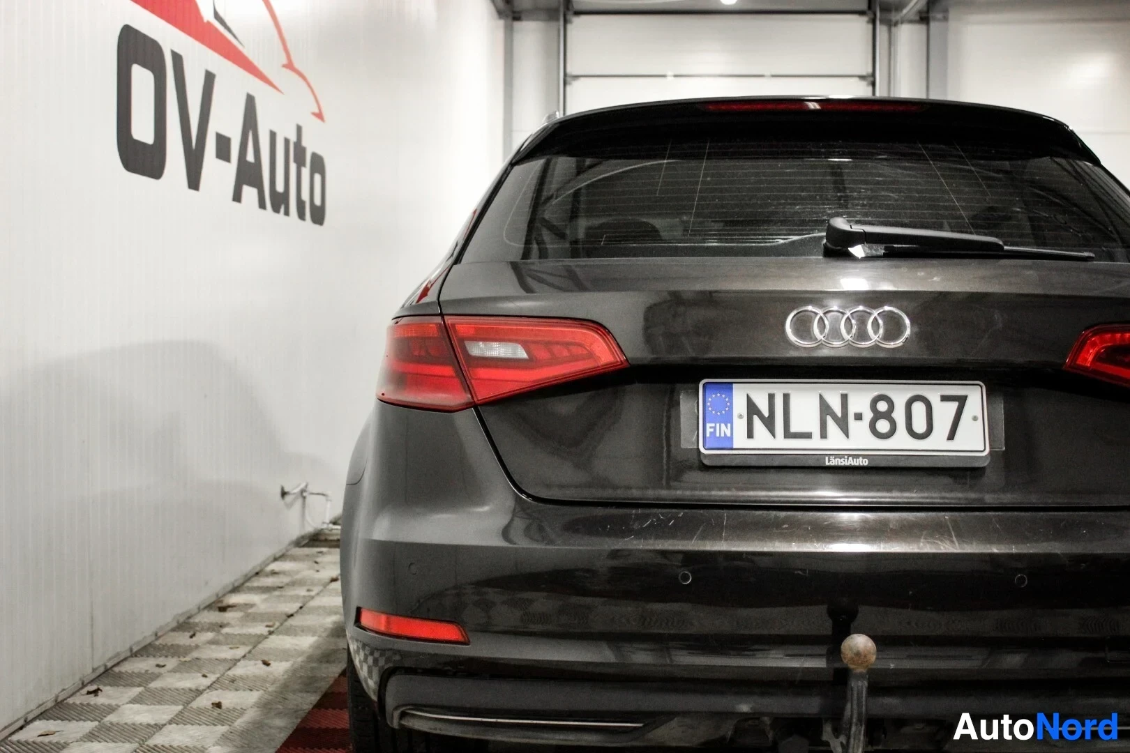Takaa: Mustan Audi A3 Sportback -auton takaosa, jossa näkyy rekisterikilpi. Takapuskurissa on vetokoukku ja pysäköintianturit. Takavalot ja takalasinpyyhin ova