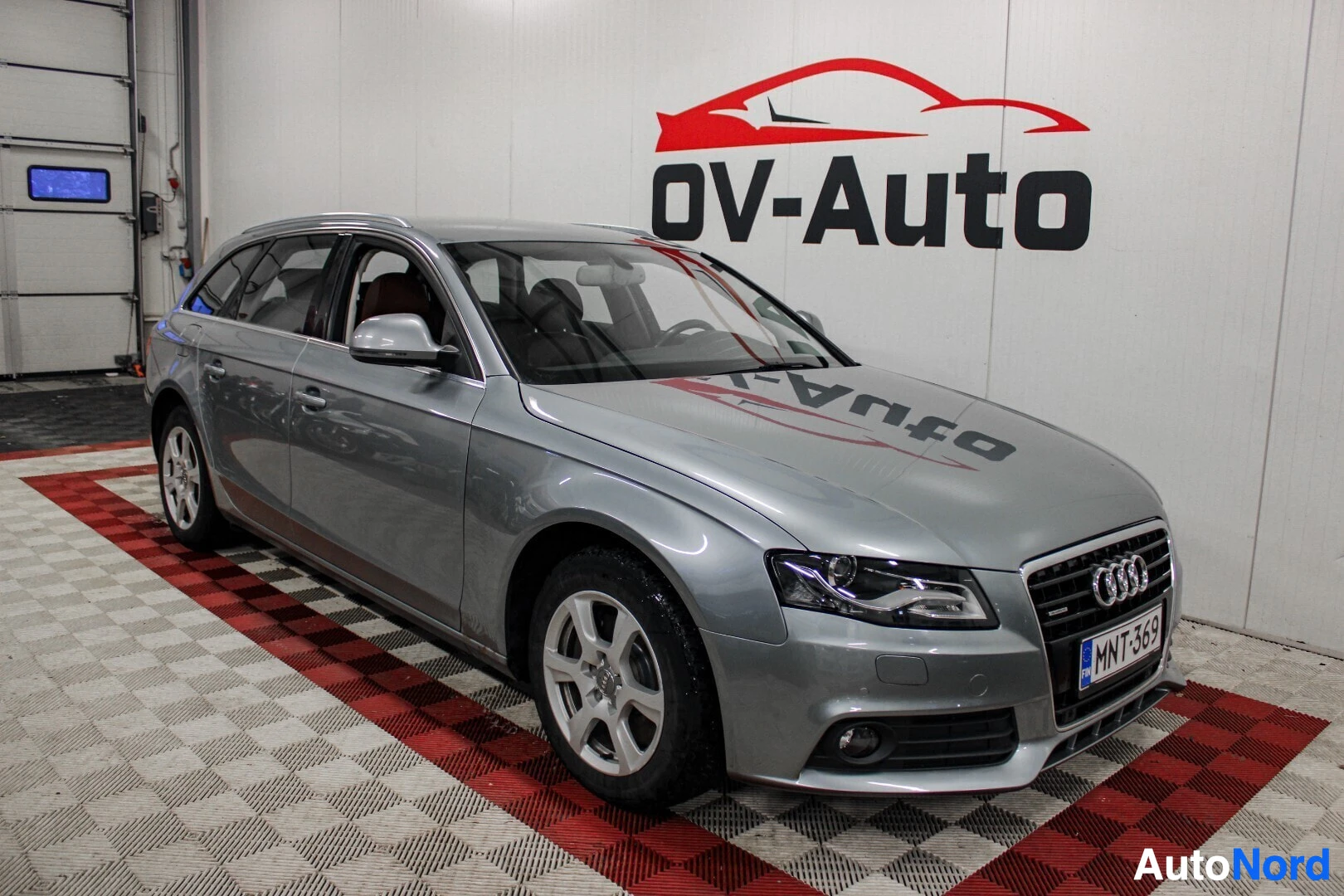 Etuviisto, nokka vasemmalle: Harmaa Audi A4 Avant -farmariauto kuvattuna etuviistosta oikealta puolelta autohallissa. Autossa on hopeanväriset vanteet. Rekisterikilpi on nä