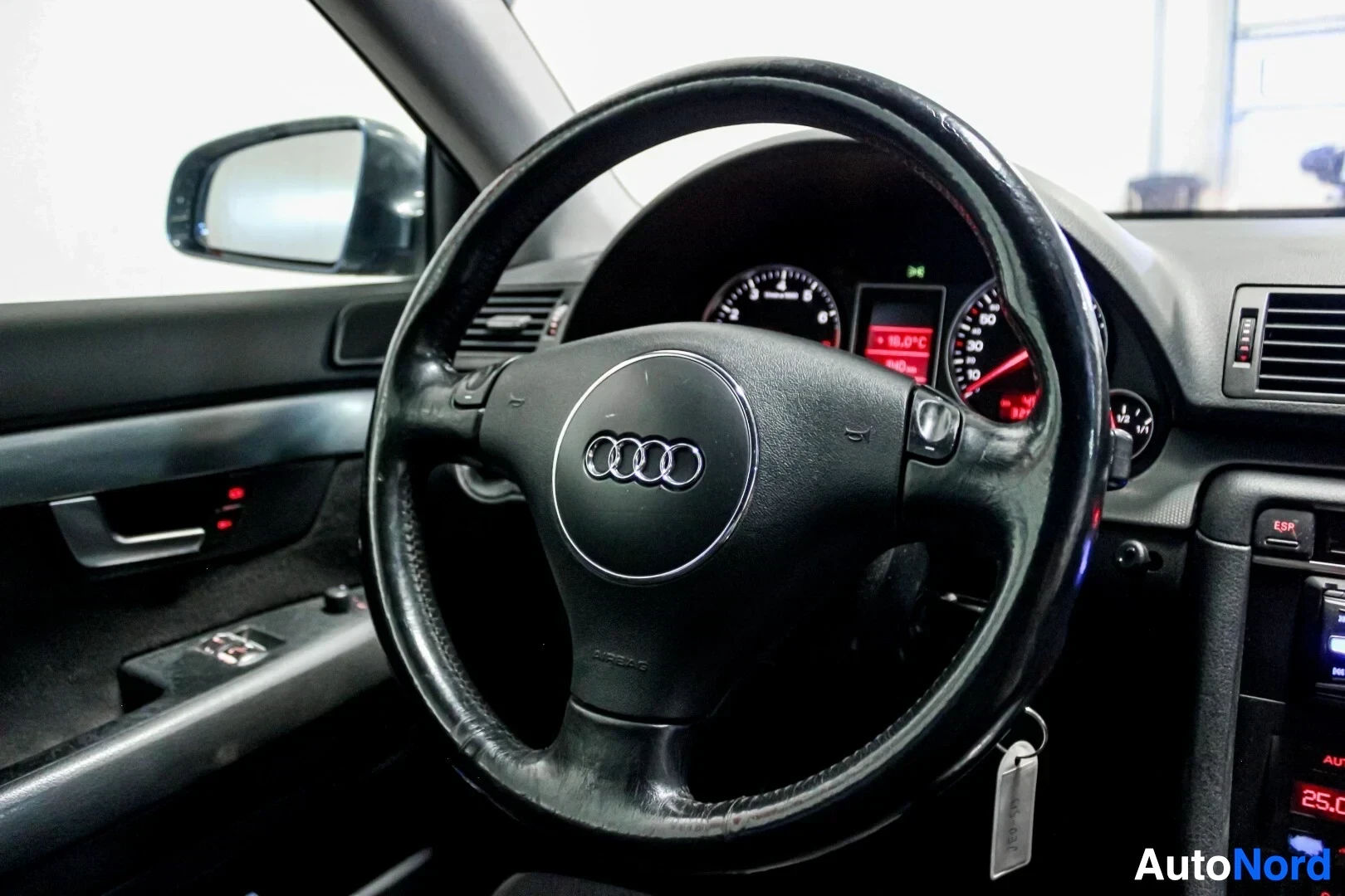 Ohjaamo: Kuva auton ohjaamosta, jossa näkyvät ohjauspyörä Audi-logolla ja mittaristo.