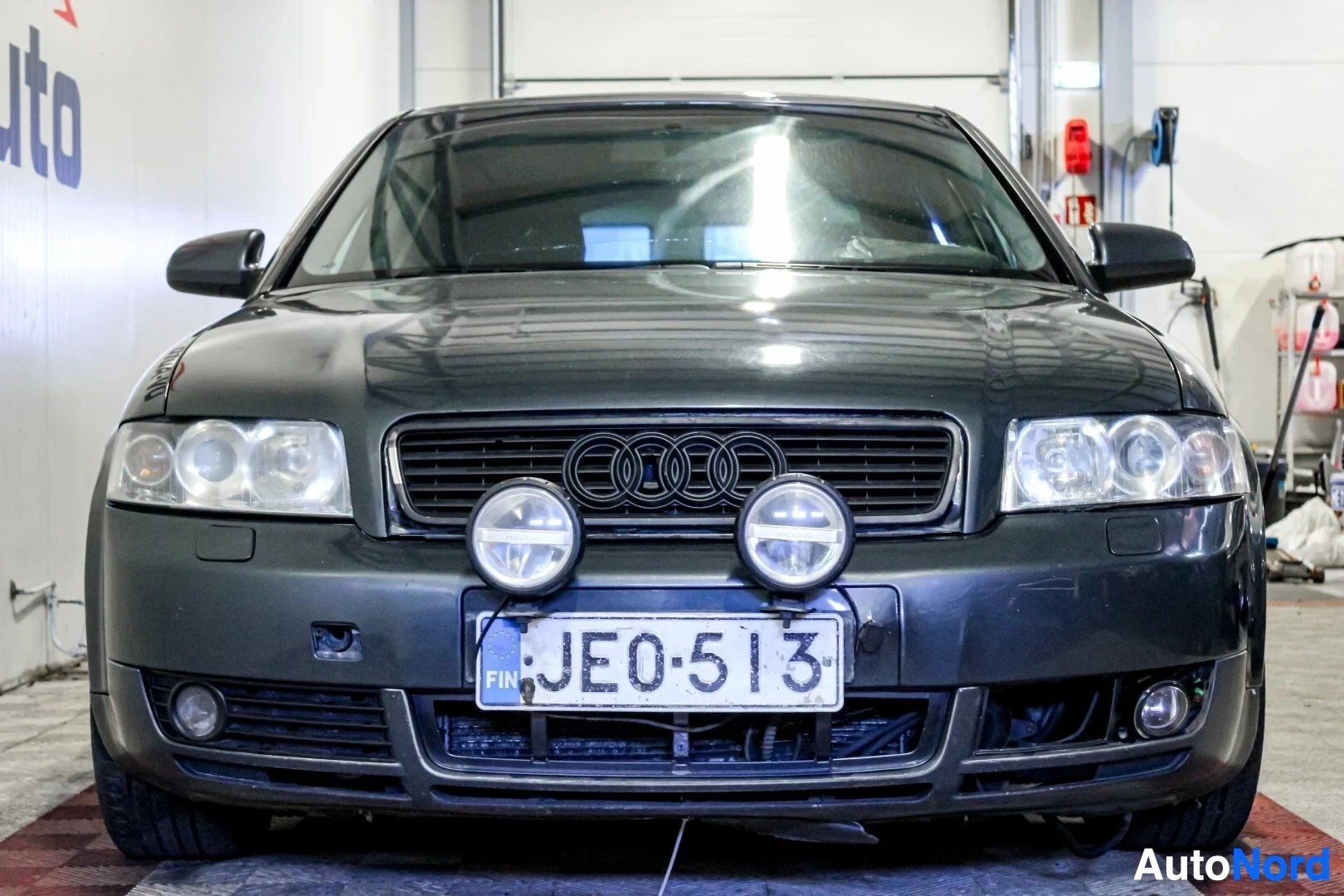 Edestä: Lähikuva tummanharmaasta Audi A4:n keulasta, jossa näkyy etusäleikkö, Audin logo, ajovalot, kaksi pyöreää lisävaloa ja rekisterikilpi