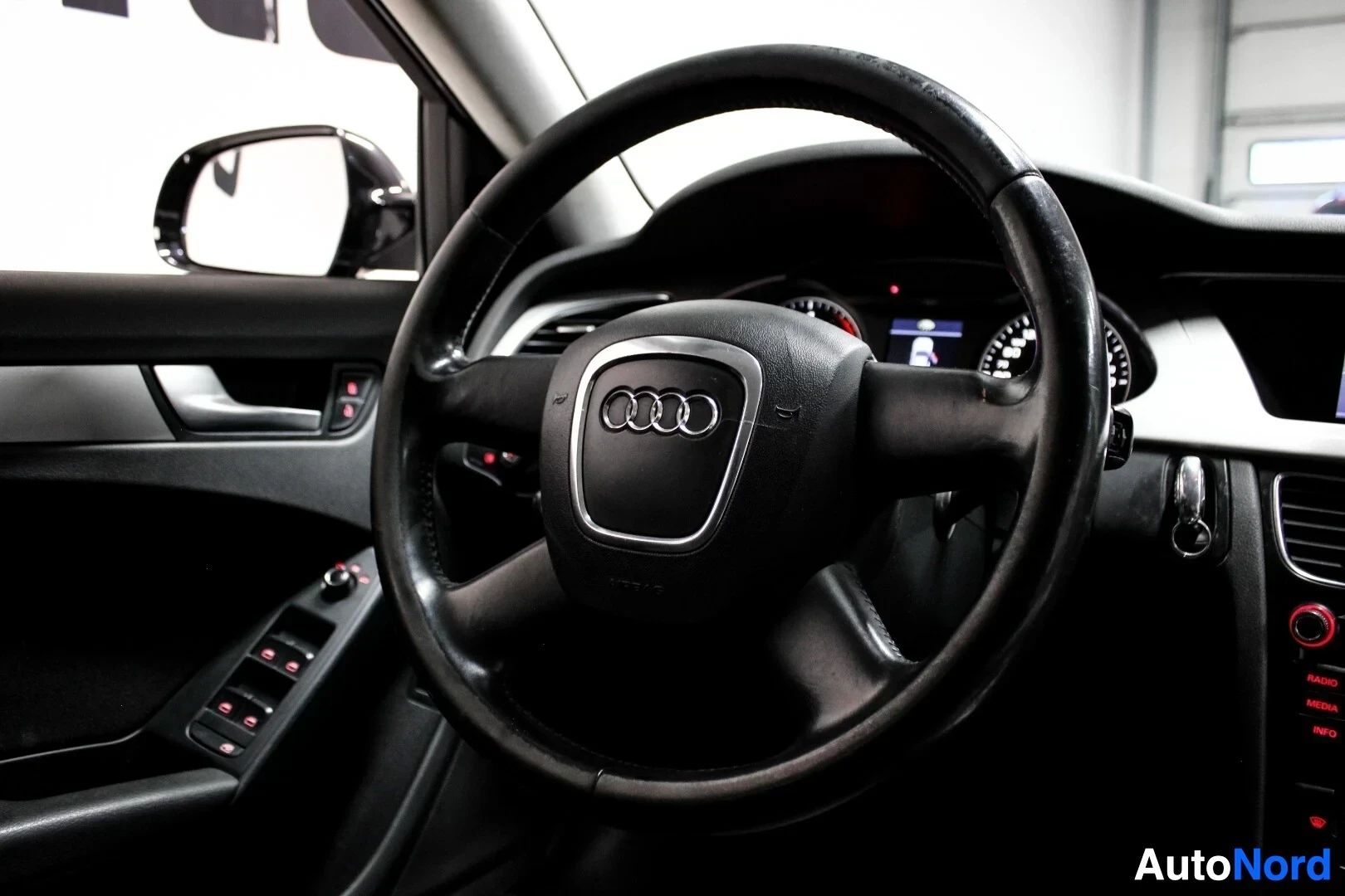 Ohjaamo: Ohjauspyörä ja mittaristo, joista ohjauspyörässä on Audi-logo keskellä.