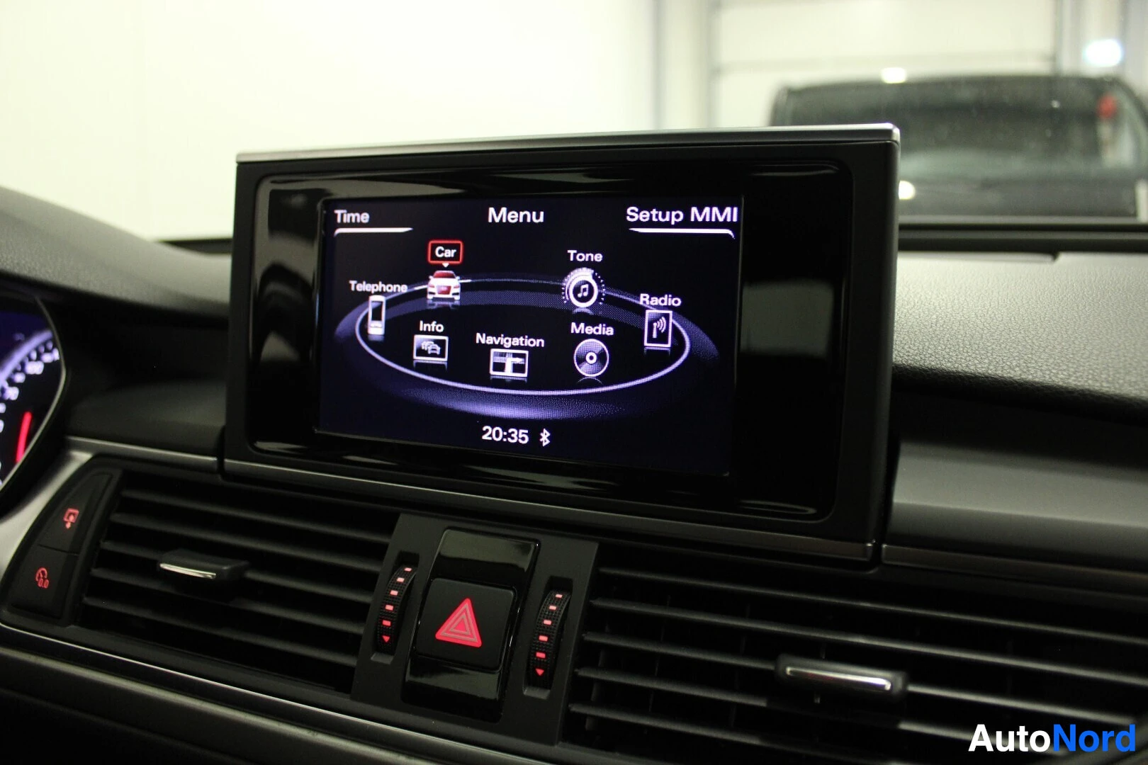 Yksityiskohta: Lähikuva auton sisätiloista, jossa näkyy auton infotainment-järjestelmän näyttö. Näytöllä on "Setup MMI"-valikko, joka näyttää kuvakkeita navigoinnille, mediall