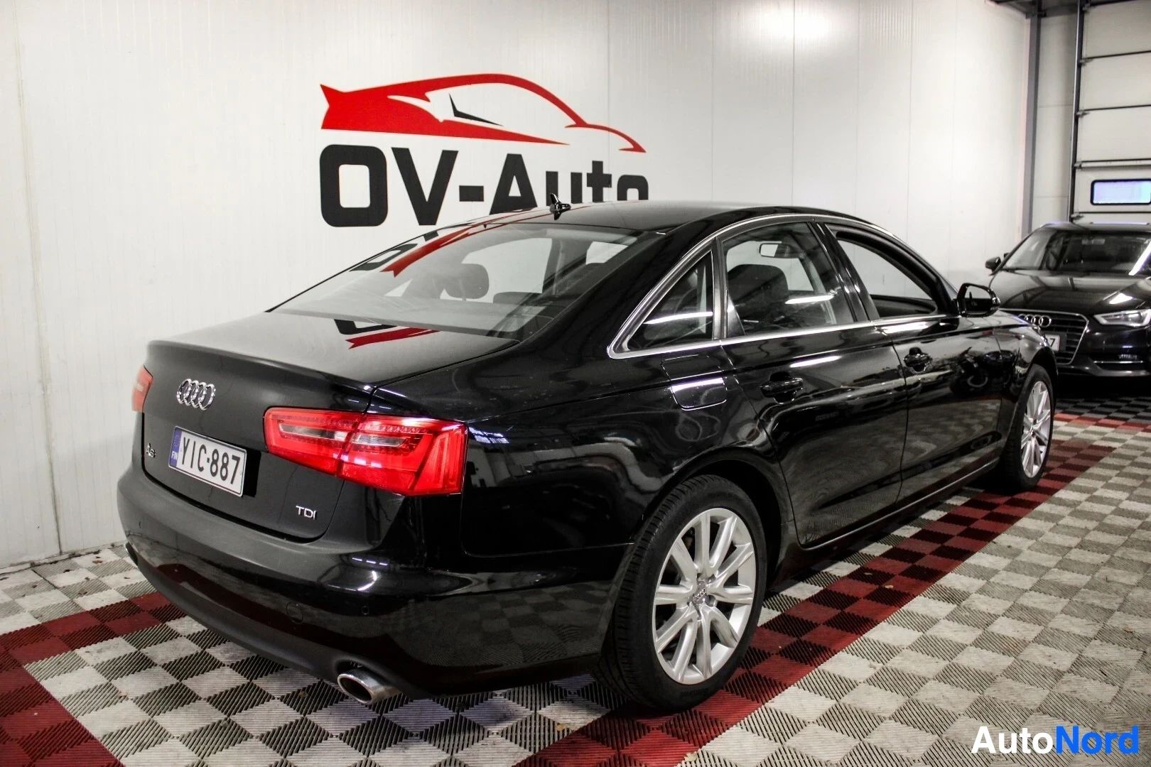 Takaviisto: Musta Audi A6 -henkilöauto takaoikealta kuvattuna, rekisterikilvessä ja takaluukussa 'A6'- ja 'TDI'-merkinnät. Autossa on hopeanväriset kevytmetallivant