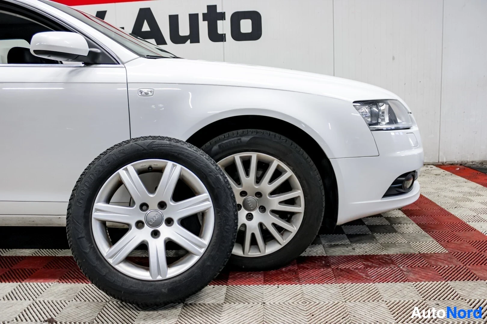 Etuviisto, nokka oikealle: Kuva auton etuosasta edessä seisovan talvirenkaan kanssa, renkaassa "Goodyear"-merkintä. Auton edessä ja pyörässä on viisipuolaiset vanteet. Auton takana