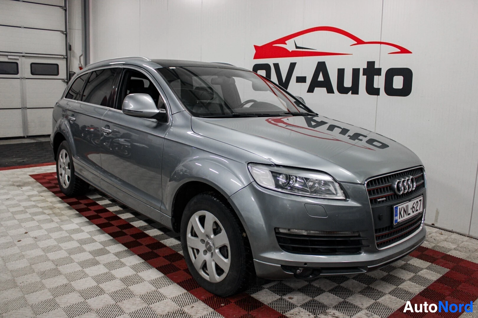 Etuviisto, nokka oikealle: Harmaa Audi Q7 etuviistosta kuvattuna sisätiloissa, rekisterikilpi.