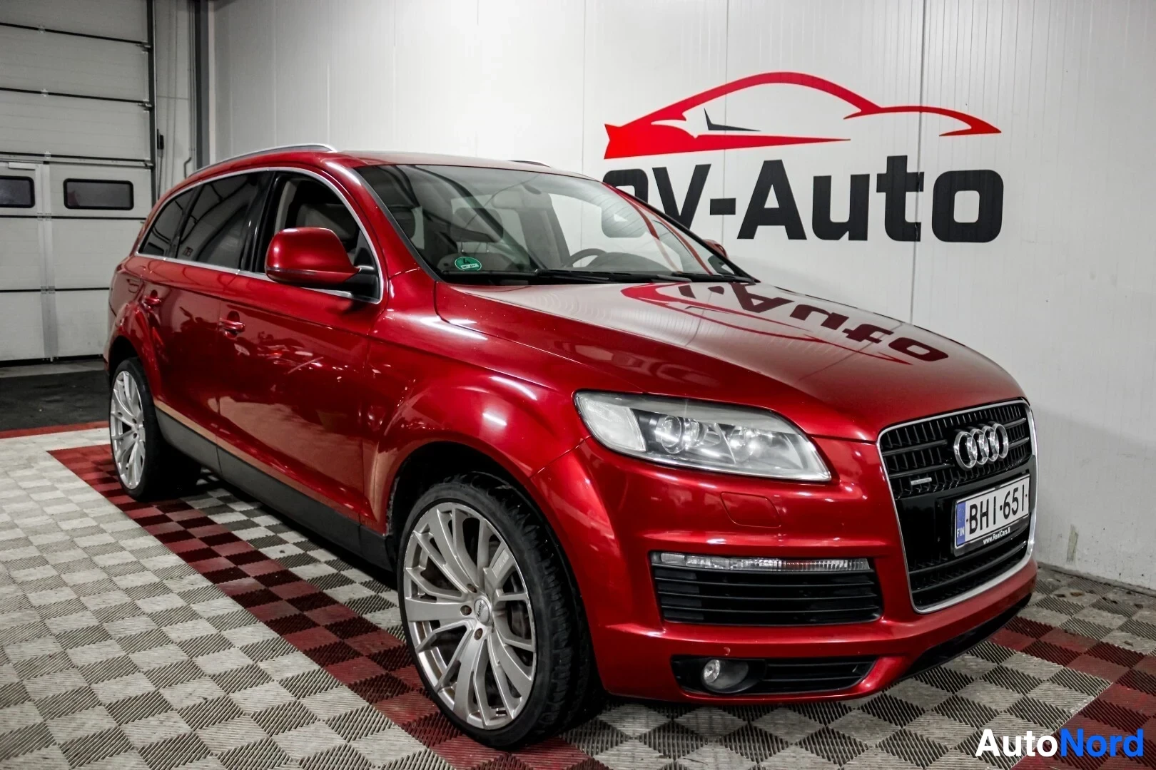 Etuviisto, nokka oikealle: Punainen Audi Q7 -maasturikuva sisätiloissa kolmivartalokulmasta, keula vasemmalla.