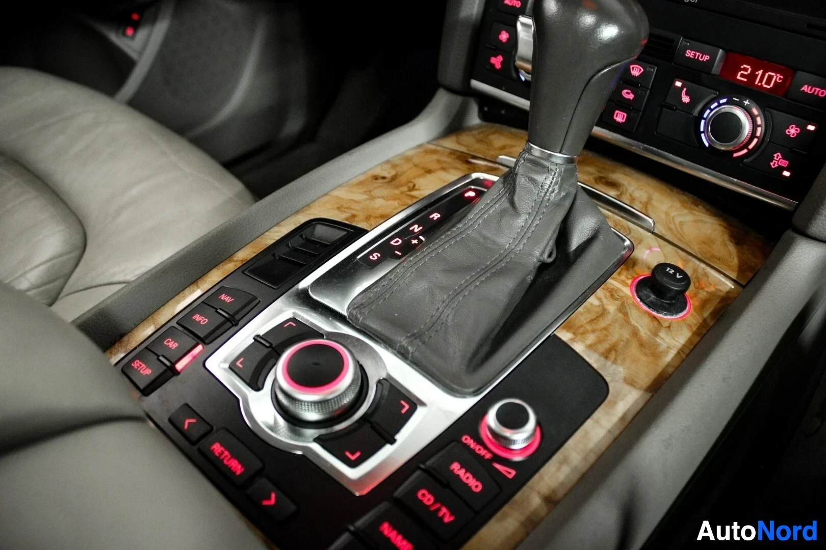 Ohjaamo: Automaattivaihteiston valitsin ja infotainment-järjestelmän säätimet puujäljitelmäpaneelissa. Näytöllä näkyy lämpötila 21.0 celsiusastetta. Käyttöpaneelissa on