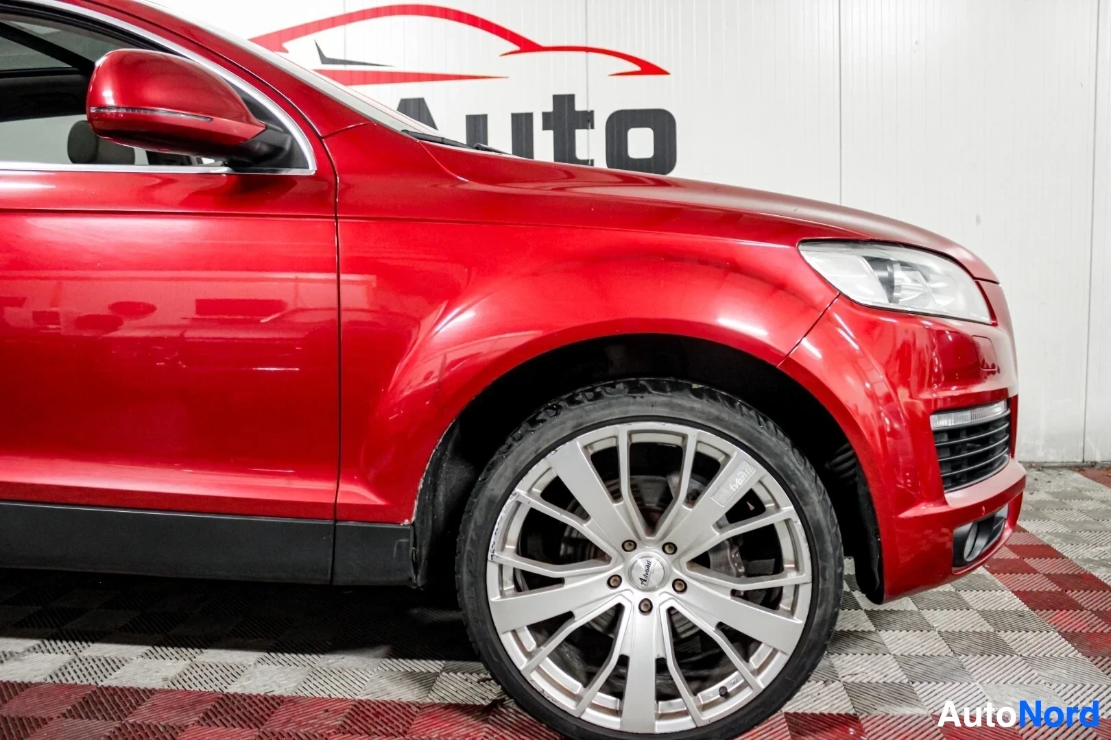Etuviisto, nokka oikealle: Punaisen Audi Q7:n etuosa ja oikea kylki kuvattuna auton edestä oikealta puolelta. Autossa on hopeanväriset monipuolaiset kevytmetallivanteet ja matalapr