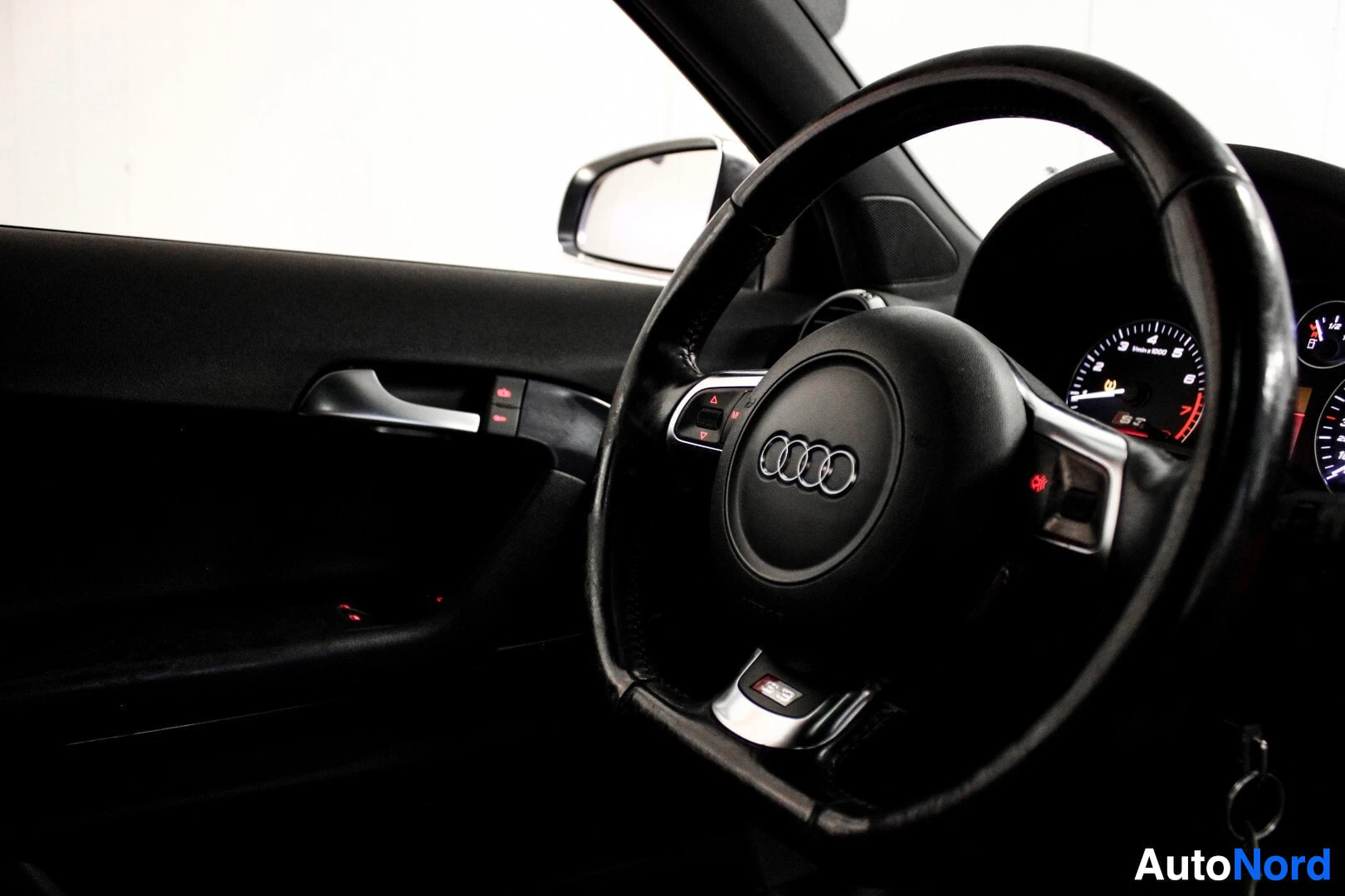 Ohjaamo: Ohjauspyörä ja vasen ovipaneeli kuvattuna viistosti takaa. Ohjauspyörässä Audi-logo ja S-logo.