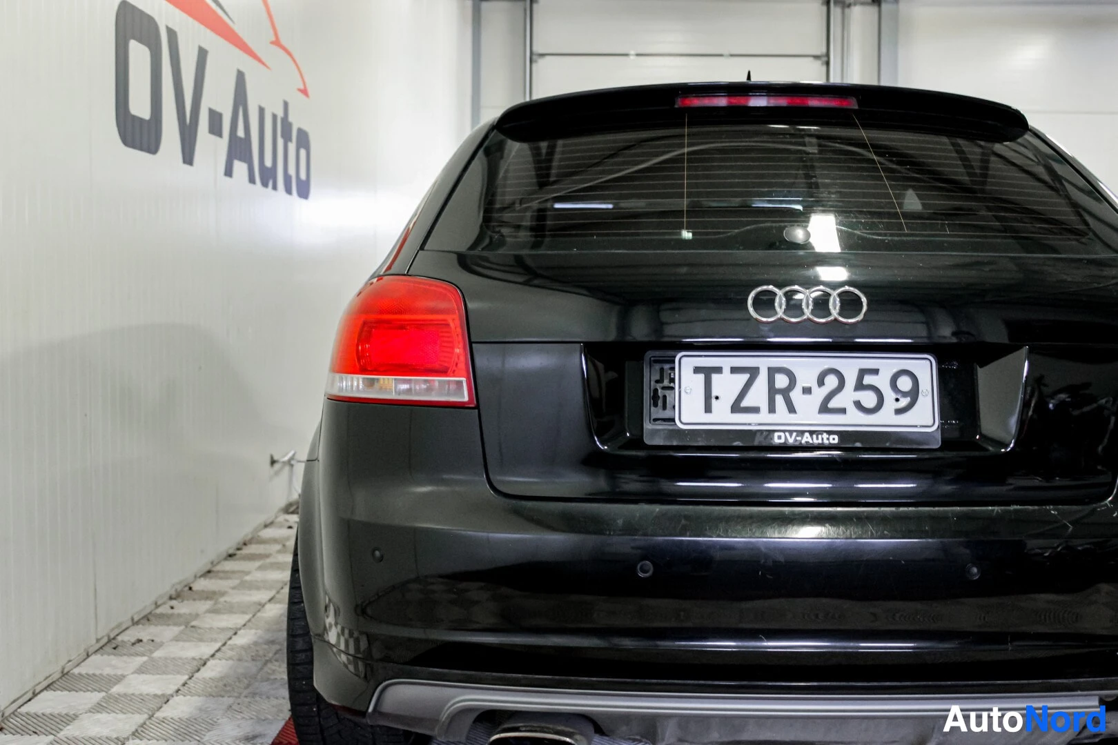 Takaa: Auton takaosa, jossa rekisterikilpi, Audi-logot ja perävalot, on kuvattu suoraan takaa. Takapuskurissa on pysäköintitutkan antureita ja alareunassa näky