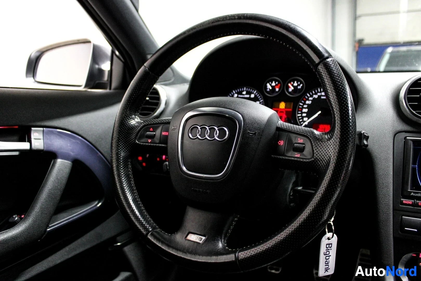 Yksityiskohta: Lähikuva auton perforoidusta nahkapäällysteisestä ohjauspyörästä, jossa on Audi-logo ja punaiset ompeleet. Ohjauspyörän alaosaan on kaiverrettu 'S3'.