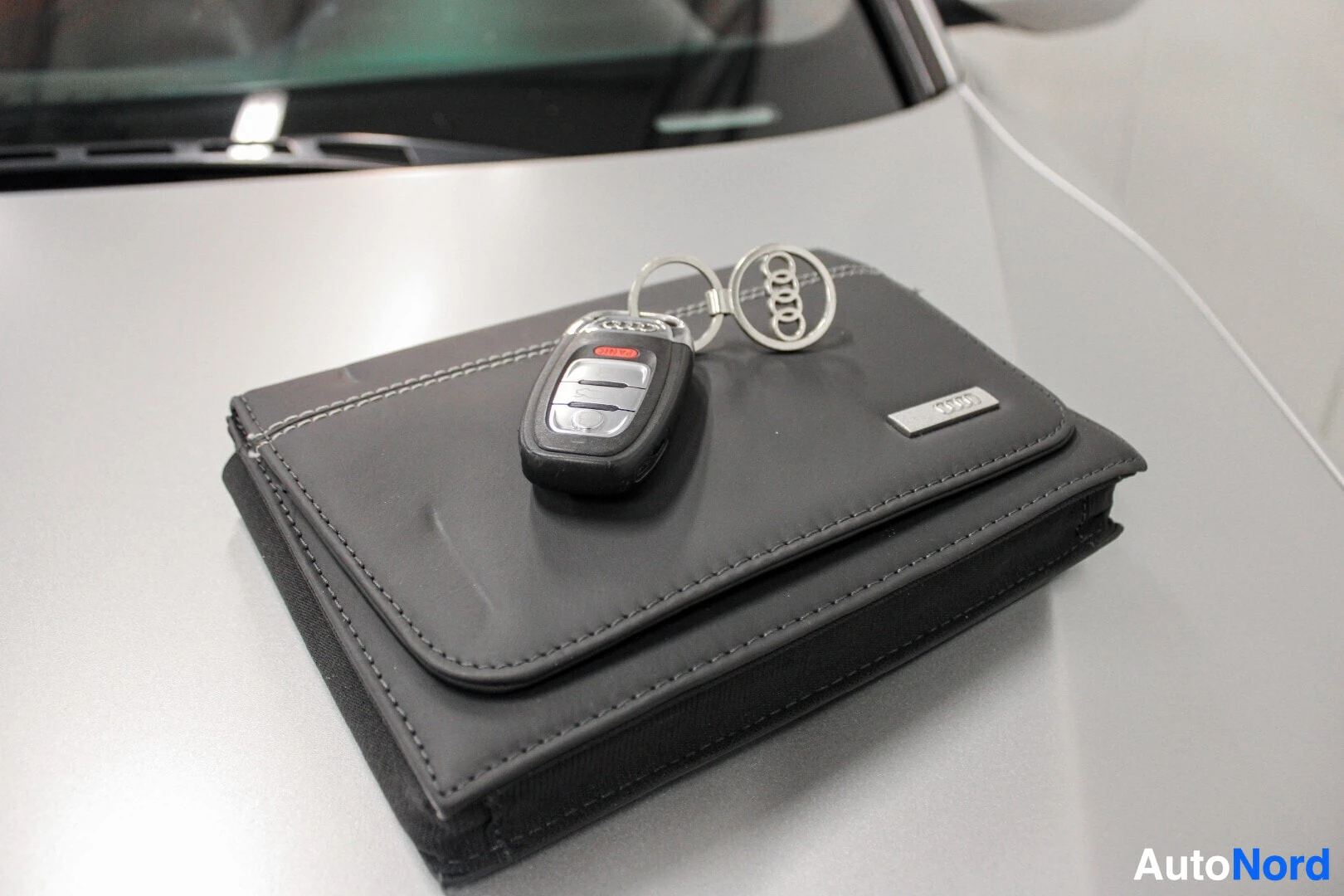 Yksityiskohta: Lähikuva avaimista ja Audi-ohjekirjan kotelosta auton konepellillä.