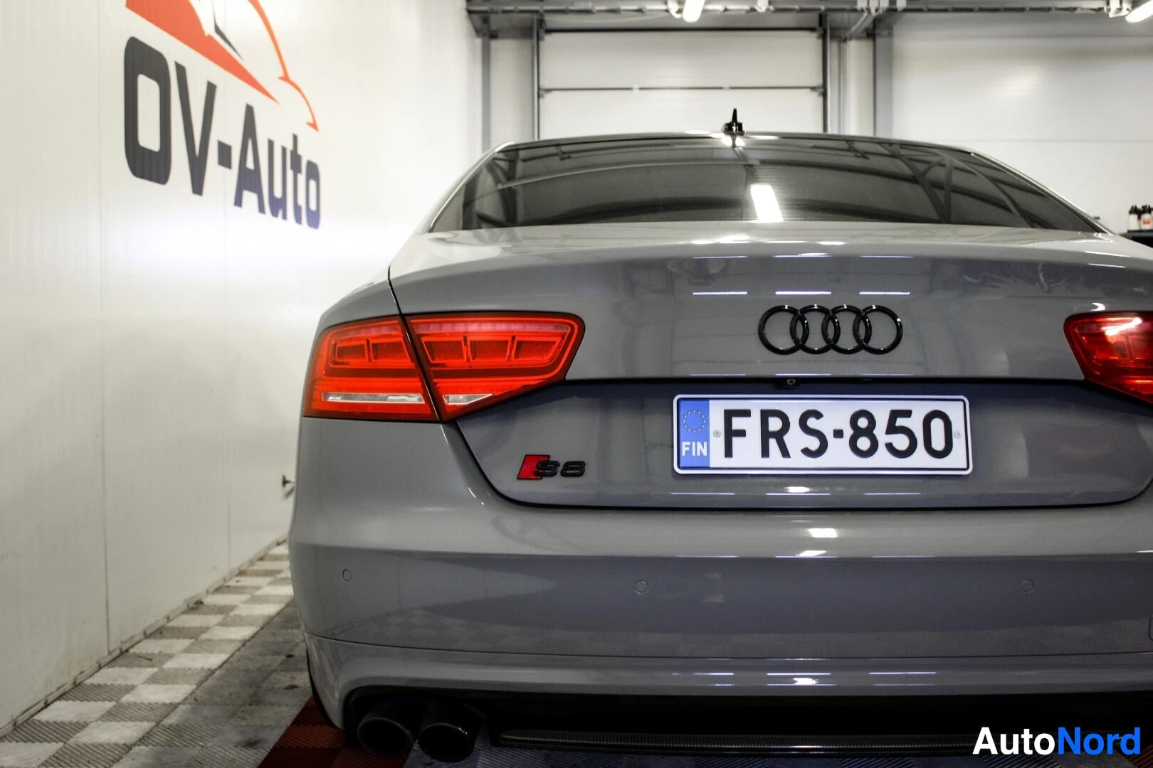 Takaa: Lähikuva henkilöauton perästä, rekisterikilpi ja takavalot näkyvissä. Rekisterikilven yläpuolella on Audi-logo ja alapuolella S8-merkki.