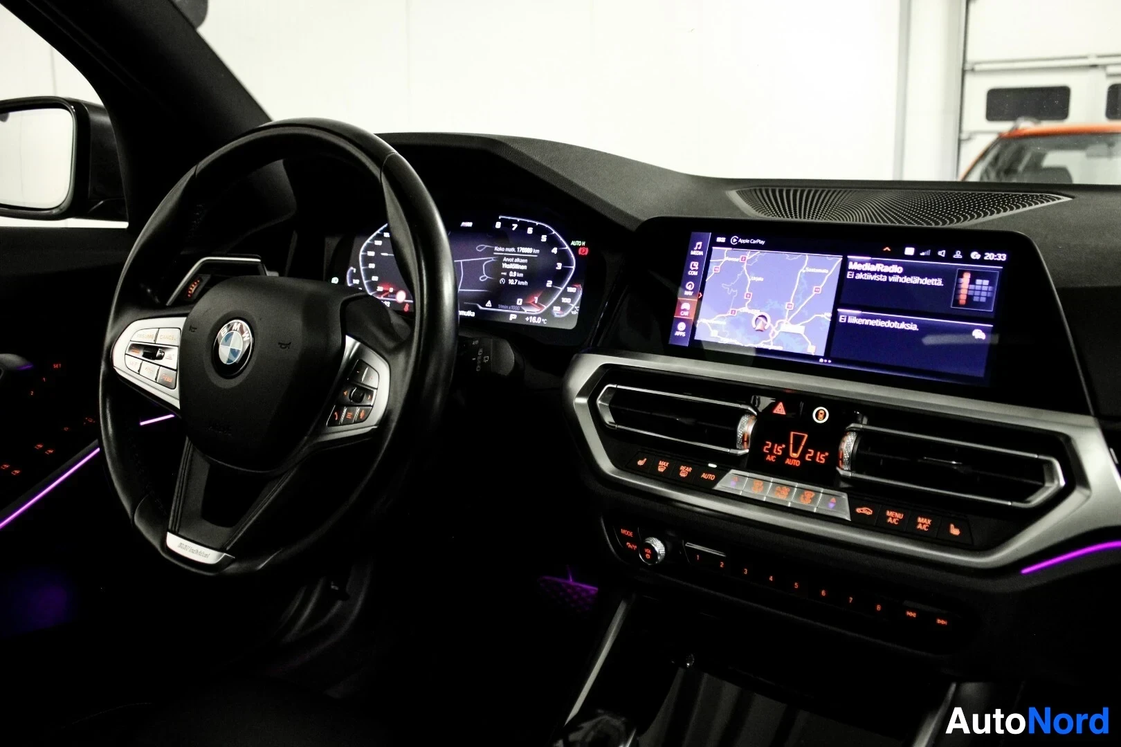Ohjaamo: Lähikuva auton ohjaamosta kuljettajan puolelta, jossa näkyvät BMW-logolla varustettu monitoimiohjauspyörä, digitaalinen mittaristo nopeuslukemalla 0 km/h ja kes