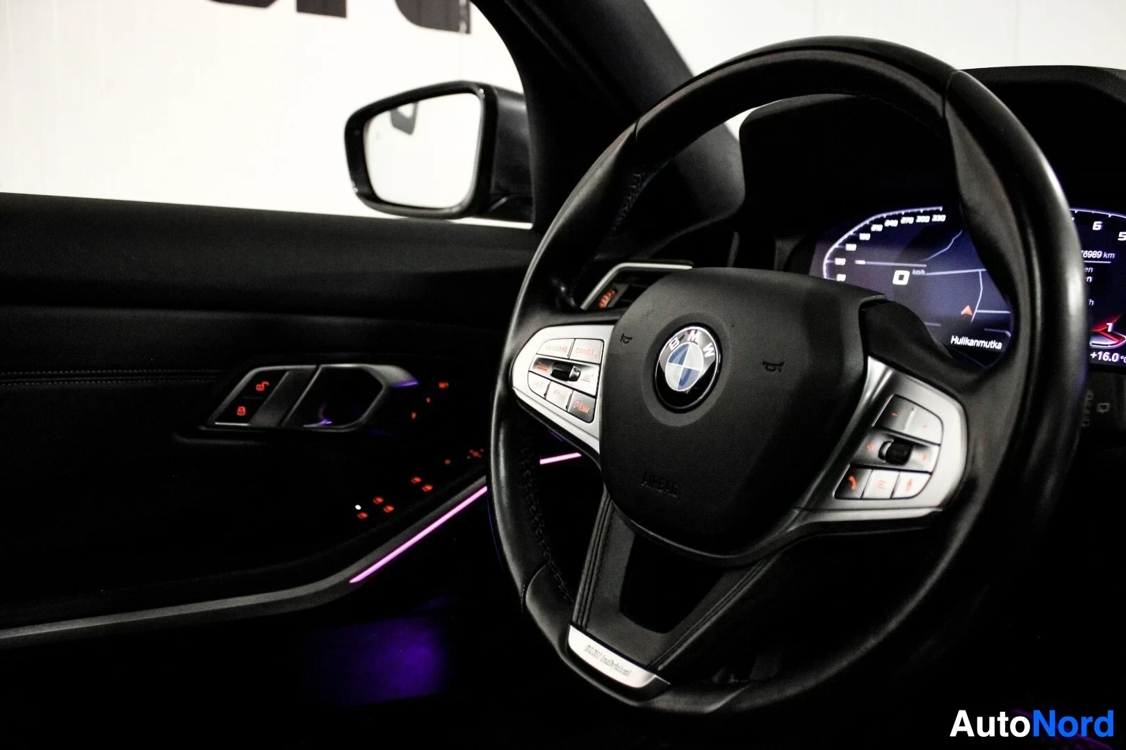 Yksityiskohta: Lähikuva auton ohjauspyörästä ja kuljettajan oven sisäpaneelista. Ohjauspyörässä on BMW-logo ja monitoiminäppäimet. Ovenkahvassa ja oviverhoilun alaosassa on pu
