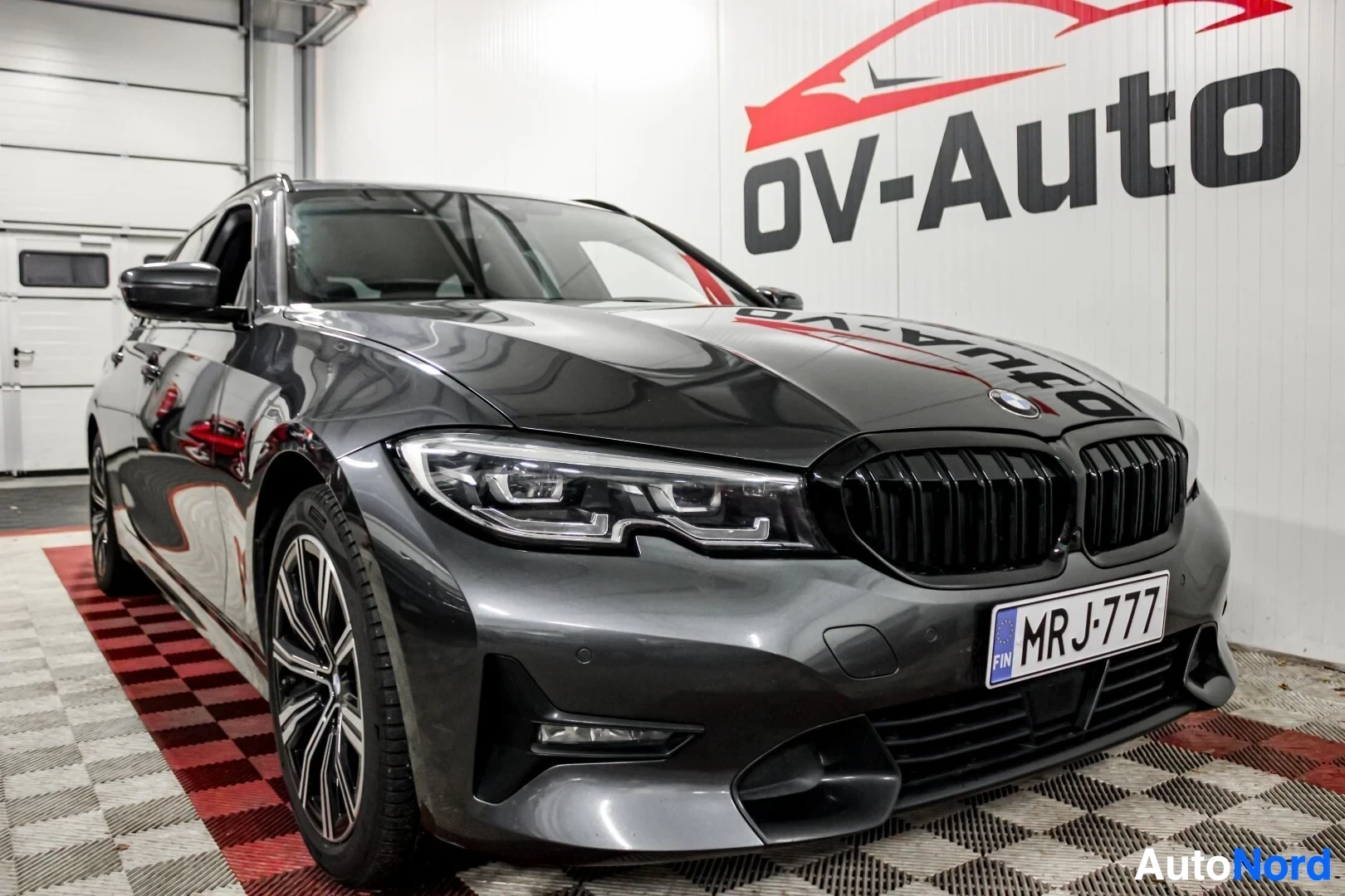 Etuviisto, nokka oikealle: Harmaa BMW 3-sarjan farmari pysäköitynä myyntihallissa, näkyy etuvasemmalta.