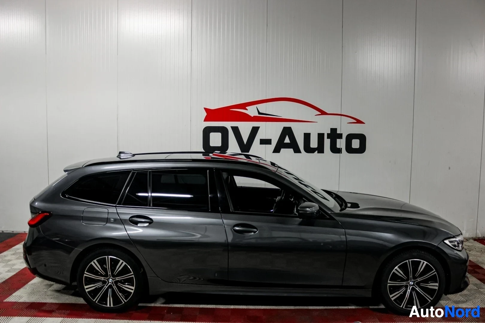 Sivulta: Tummanharmaa farmariauto kuvattuna oikealta sivulta sisätiloissa. Autossa on kattokaiteet ja monipuolaiset kevytmetallivanteet.