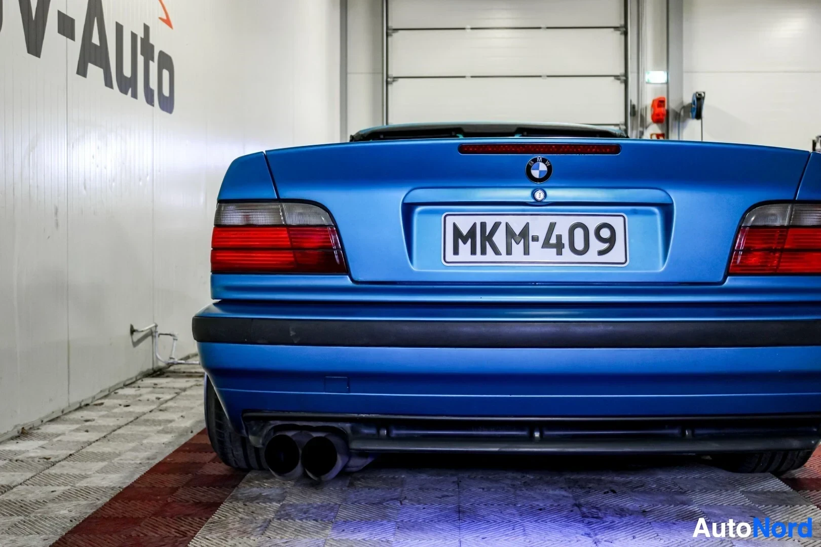 Takaa: Sinisessä autossa on kilpi "". Pakoputket ovat auton alla keskellä. BMW-logo on tavaratilan kannessa