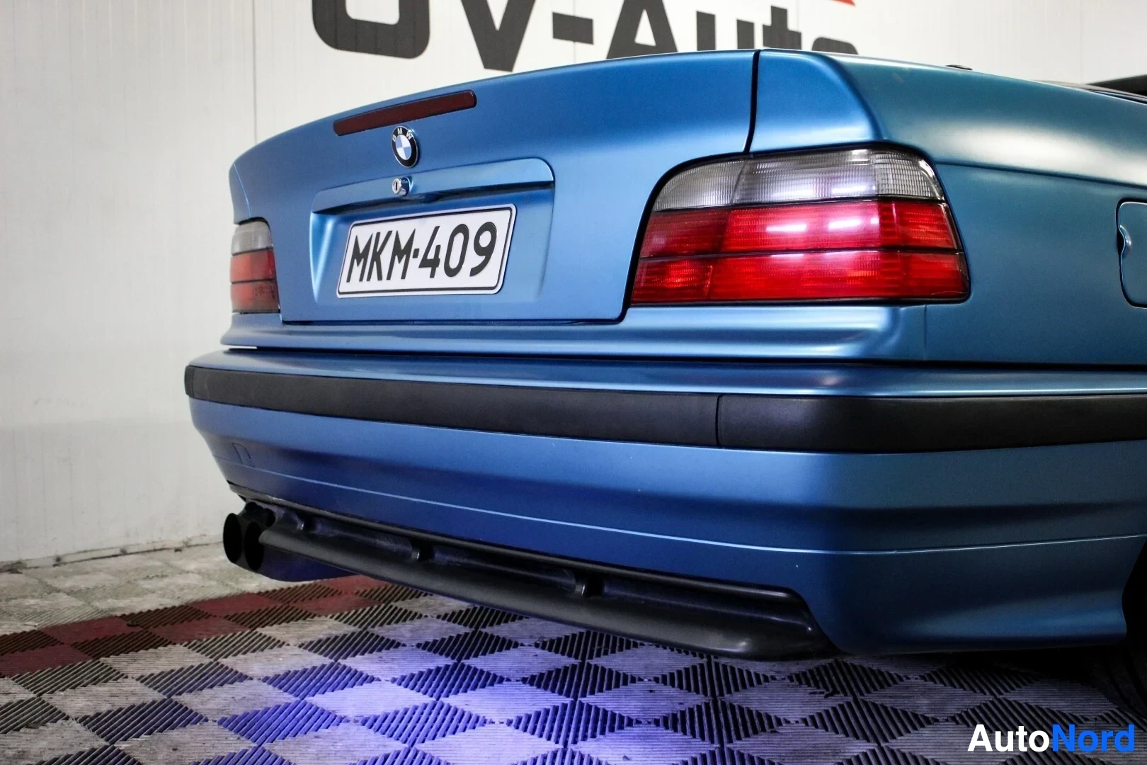 Takaviisto: Sinisessä autossa on kilpi "" ja BMW-logo tavaratilan kannessa. Kuvassa näkyy auton peräosan oikea puoli