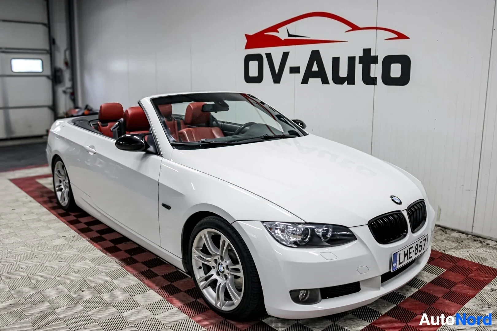 Etuviisto, nokka oikealle: Valkoinen avokori BMW -coupé-katto auki, etukulma oikealta, punaiset penkit näkyvissä sisätiloissa.